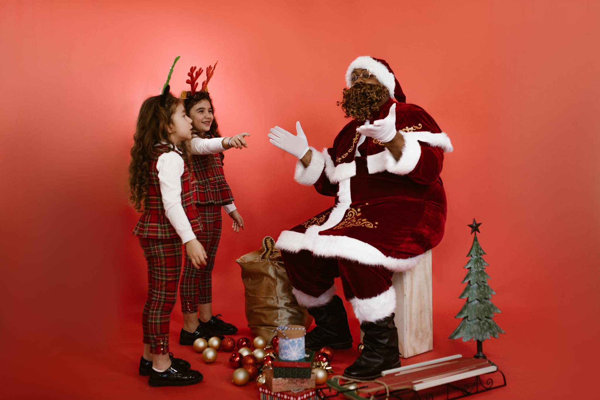 Children in Christmas attire interacting with Santa against a red background.